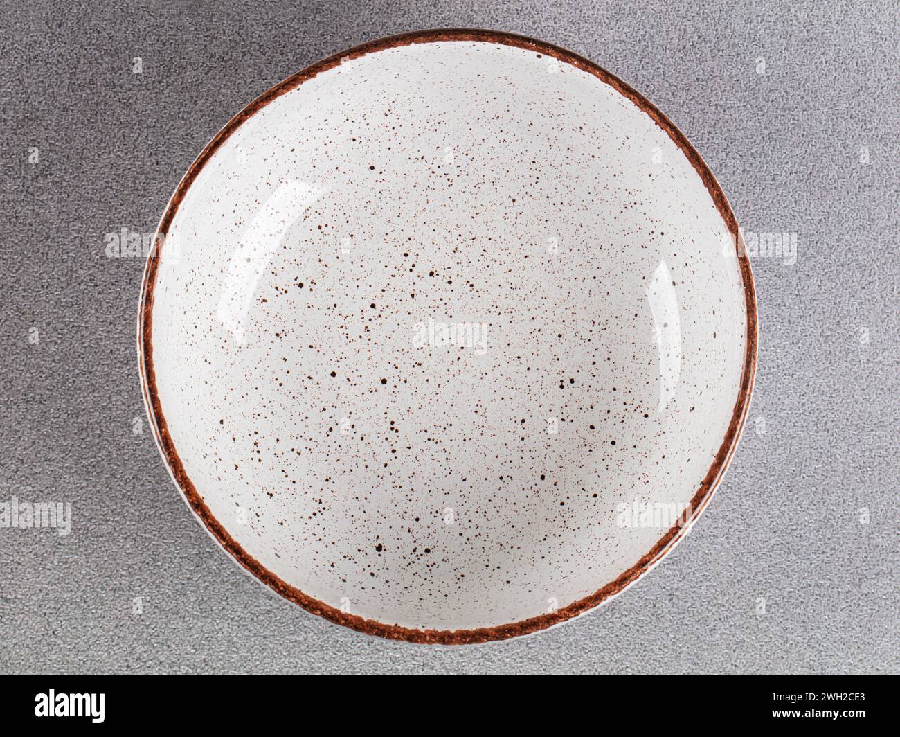 White empty deep clay plate with a spoon on a gray background. Stock Photo