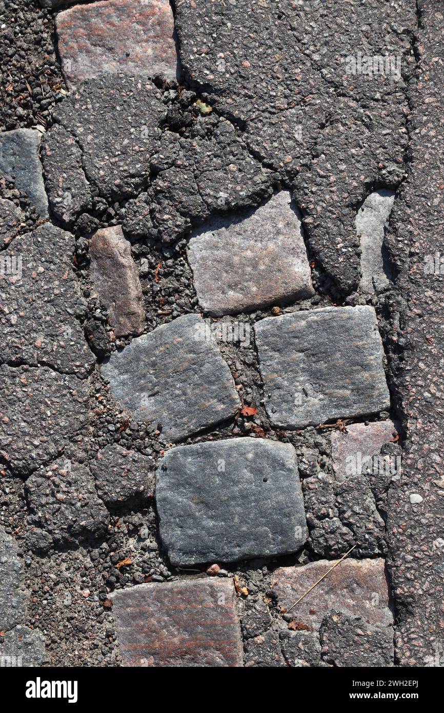 Damaged street surface in Gothenburg, Sweden. Historic cobblestone underneath layer of modern asphalt pavement. Stock Photo