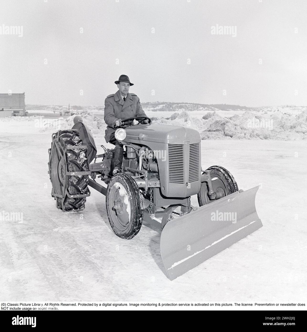 Ferguson tractor in the 1950s. A driver on the iconic Ferguson tractor featured with caterpillar bands and a snow plow in front. The Ferguson tractors were the first modern agricultural tractors and its three poinkt linkage system was a major development.   1951. Kristoffersson ref BB46-3 Stock Photo