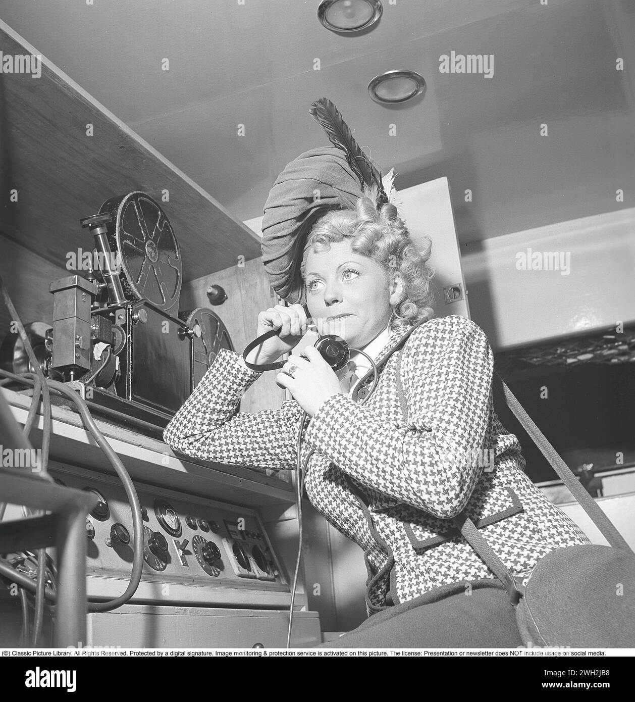 Women's fashion in the 1940s. A young woman dressed in a plaid patterned jacket and a matching hat. Pictured listening to something on the earphones. She is actress Dioris Söderström. Sweden 1945.  Kristoffersson Ref P73-5 Stock Photo