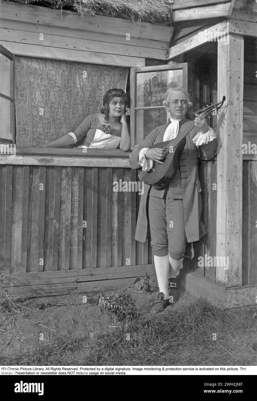 Historical event recreated. A man dressed as the famous Swedish poet Carl Michael Bellman dressed in period clothes of the 18th century playing a lute while a woman stands in the window next to him and listens. Hagateatern Stockholm 1930s Stock Photo