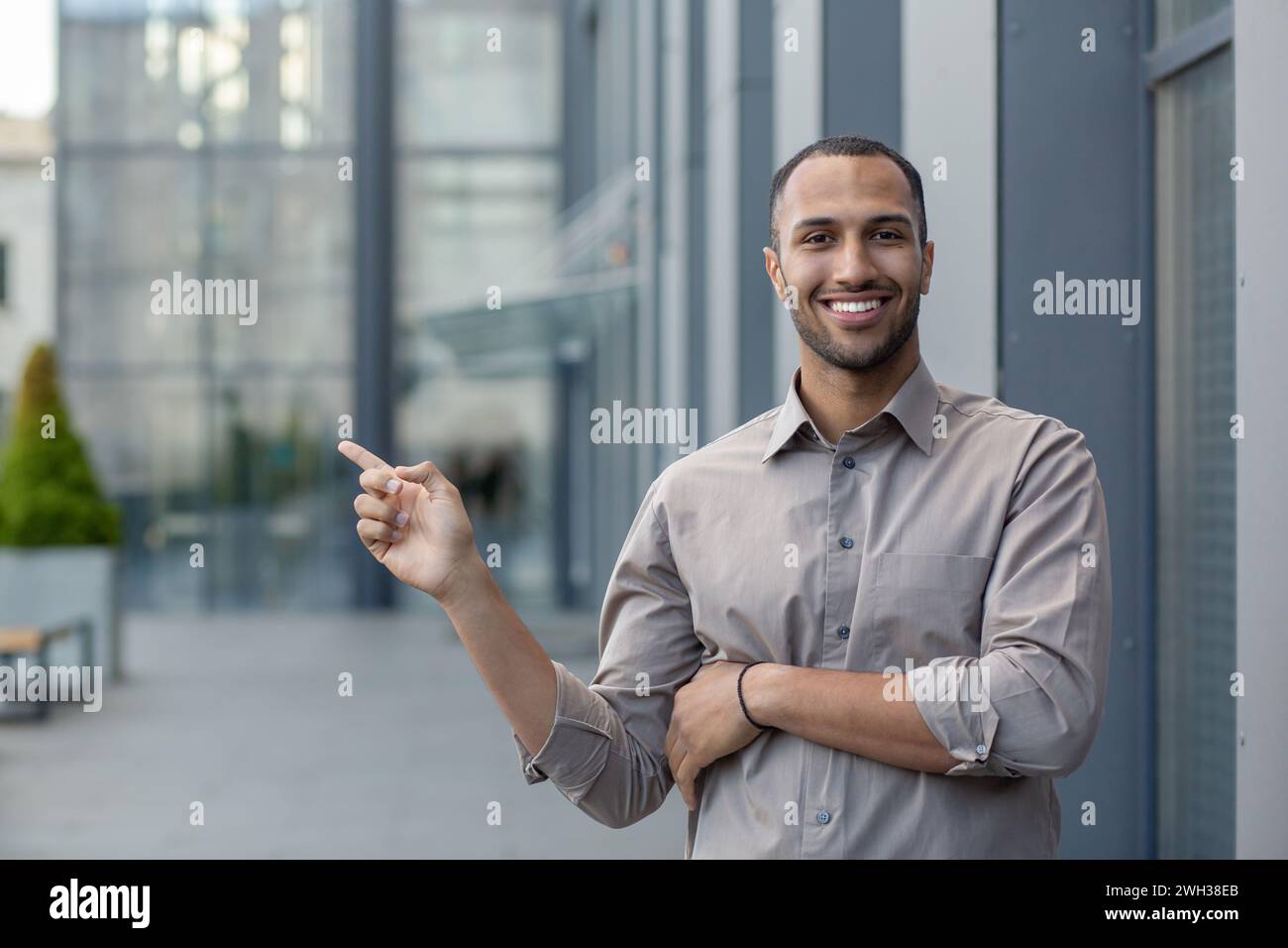 Handsome latino man with short haircut pointing with finger aside at empty space while smiling toothy at camera. Successful entrepreneur advising and praising new service for business consulting. Stock Photo