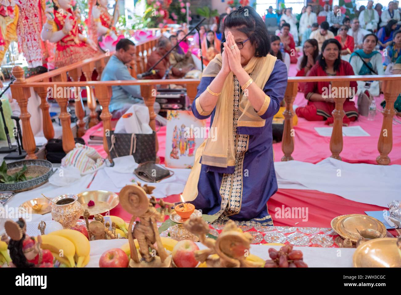A Hindu devotee prays with her hands clasped while kneeling at the altar at a temple in Jamaica, Queens, New York City. Stock Photo