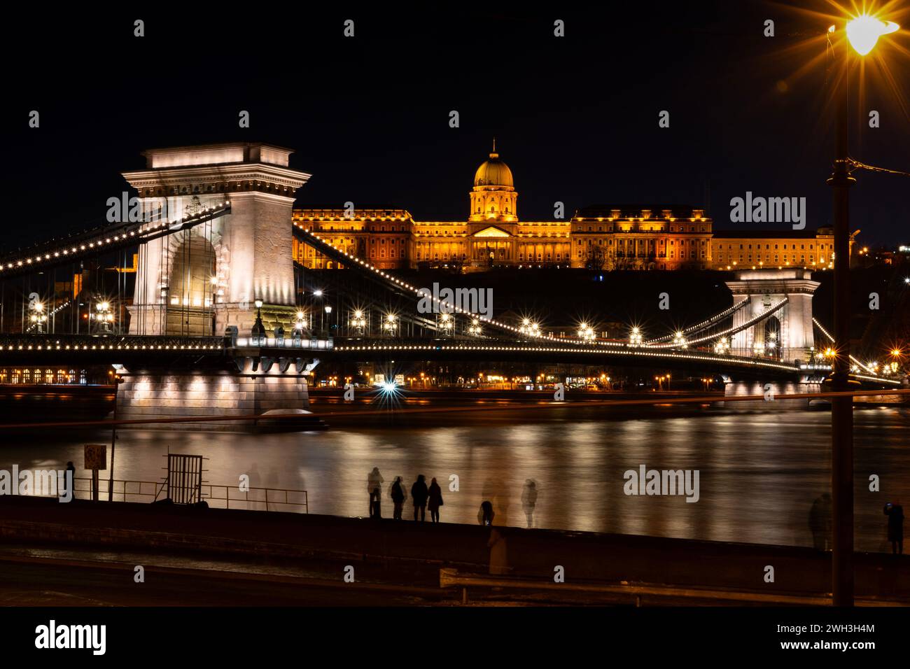 The historic Chain Bridge in Budapest lit up with lights at night on 30.12.2023. In the background is the historical Buda castle district. Stock Photo