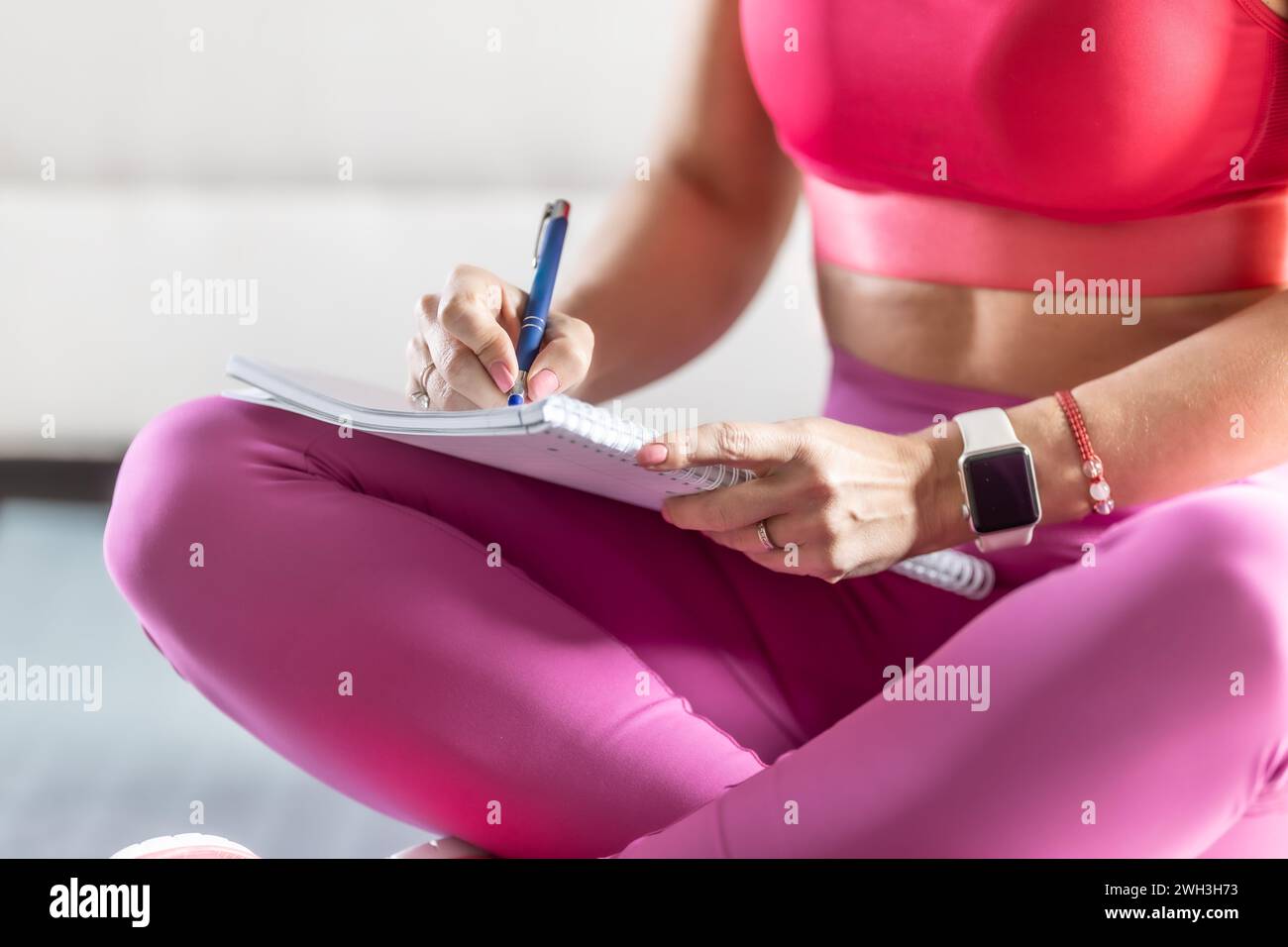 Sporty woman sits on a mat and writes down future training plans for achieving sports results. Stock Photo