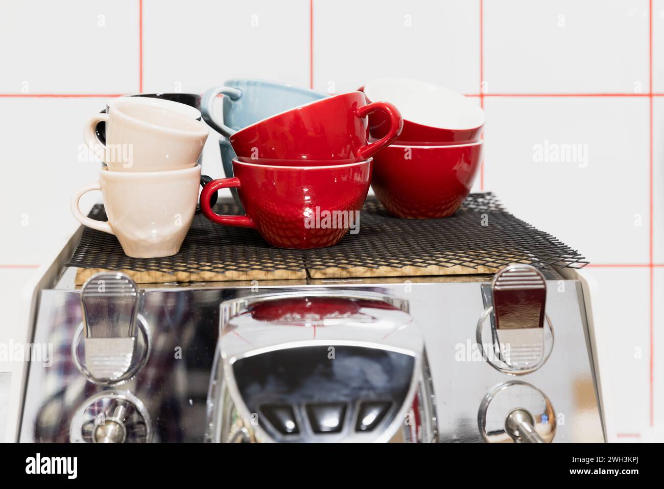 Set of colorful ceramic cups stand on a shiny steel coffee machine in front of white wall Stock Photo