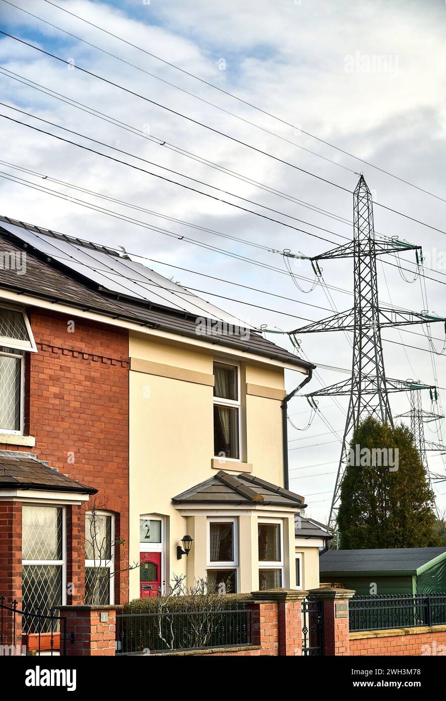 House with solar panels on roof sitting below national grid power lines and pylon showing two forms of electricity generation Stock Photo