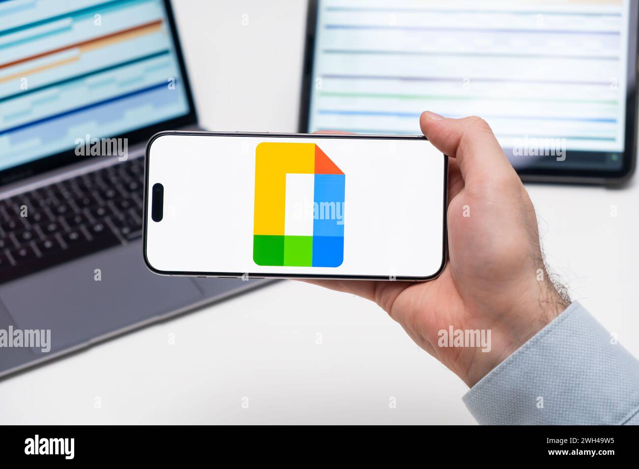 PRAGUE, CZECH REPUBLIC - JANUARY 21 2024: Google Docs logo on the screen of a cell phone in business mans hand and laptop on the background.  Stock Photo