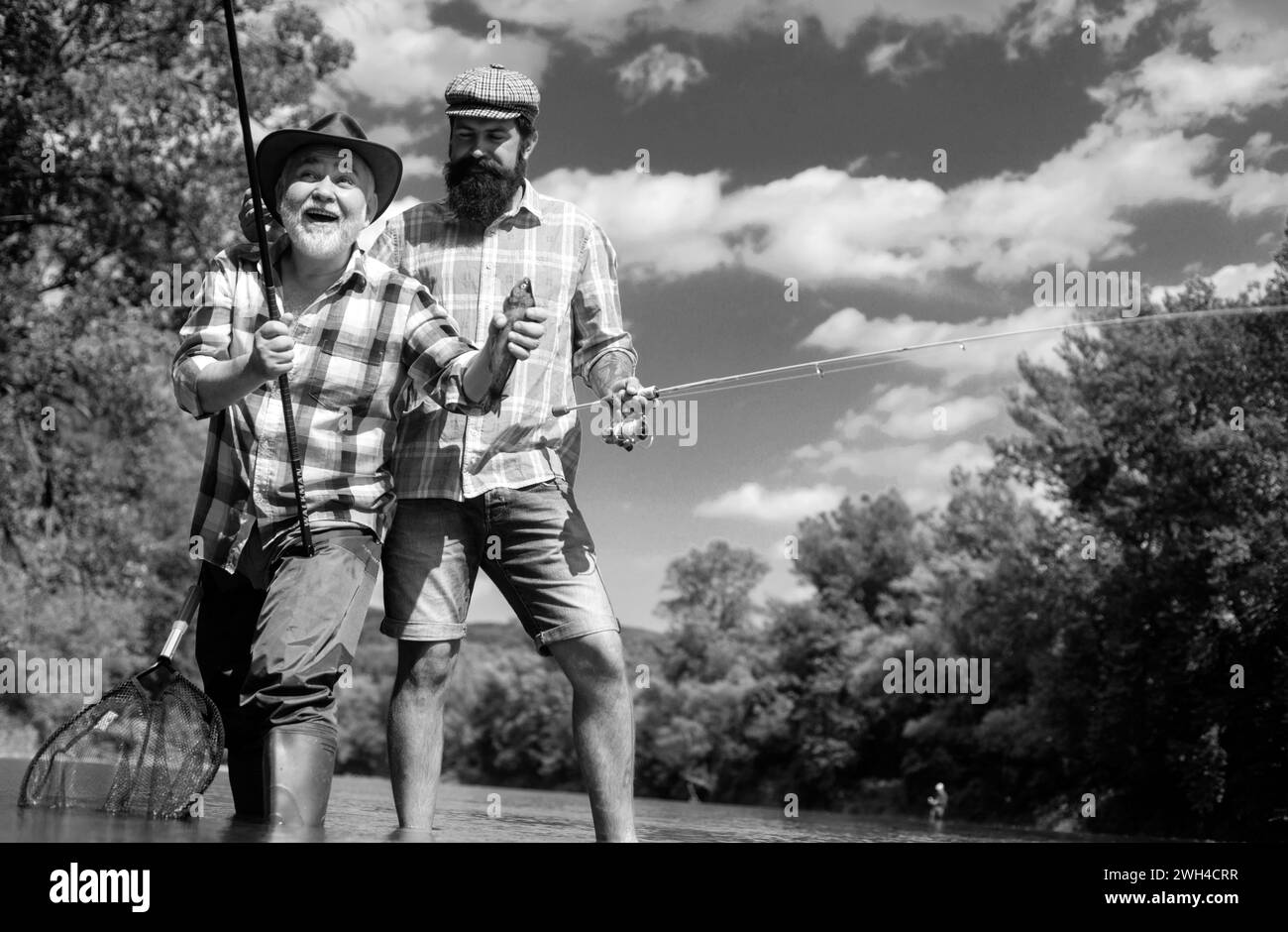 Two men friends fishing. Flyfishing angler makes cast, standing in river water. Old and young fisherman. Stock Photo