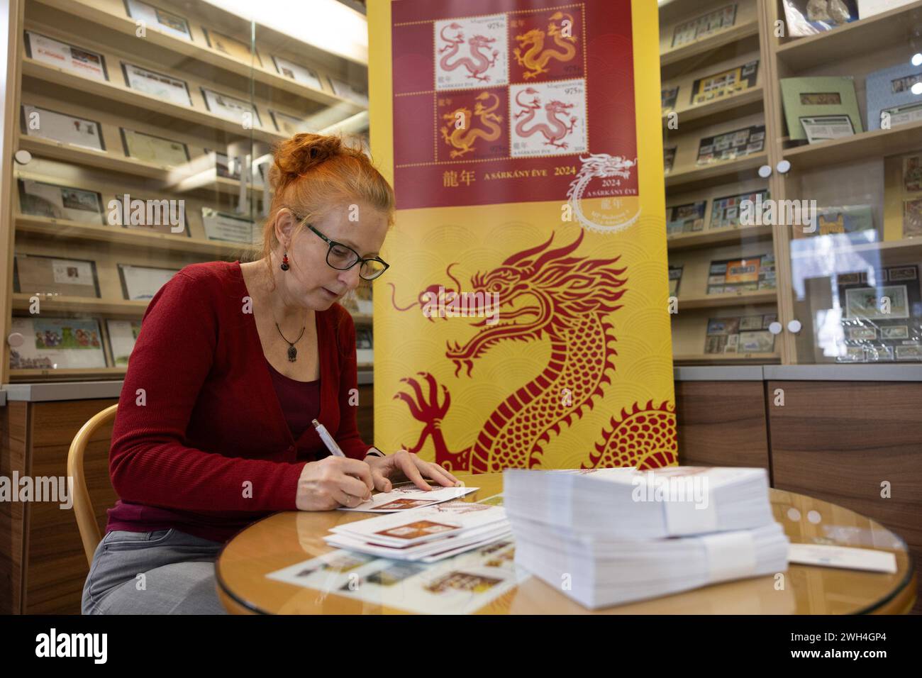 Budapest, Hungary. 7th Feb, 2024. Katalin Bodi, the Hungarian designer of the Year of the Dragon commemorative stamp recently issued by the Hungarian Post, signs on a first-day cover with the stamps of the Year of the Dragon in Budapest, Hungary, on Feb. 7, 2024. Katalin Bodi said she hoped her work could help deepen the connection between Hungary and China. Credit: Attila Volgyi/Xinhua/Alamy Live News Stock Photo