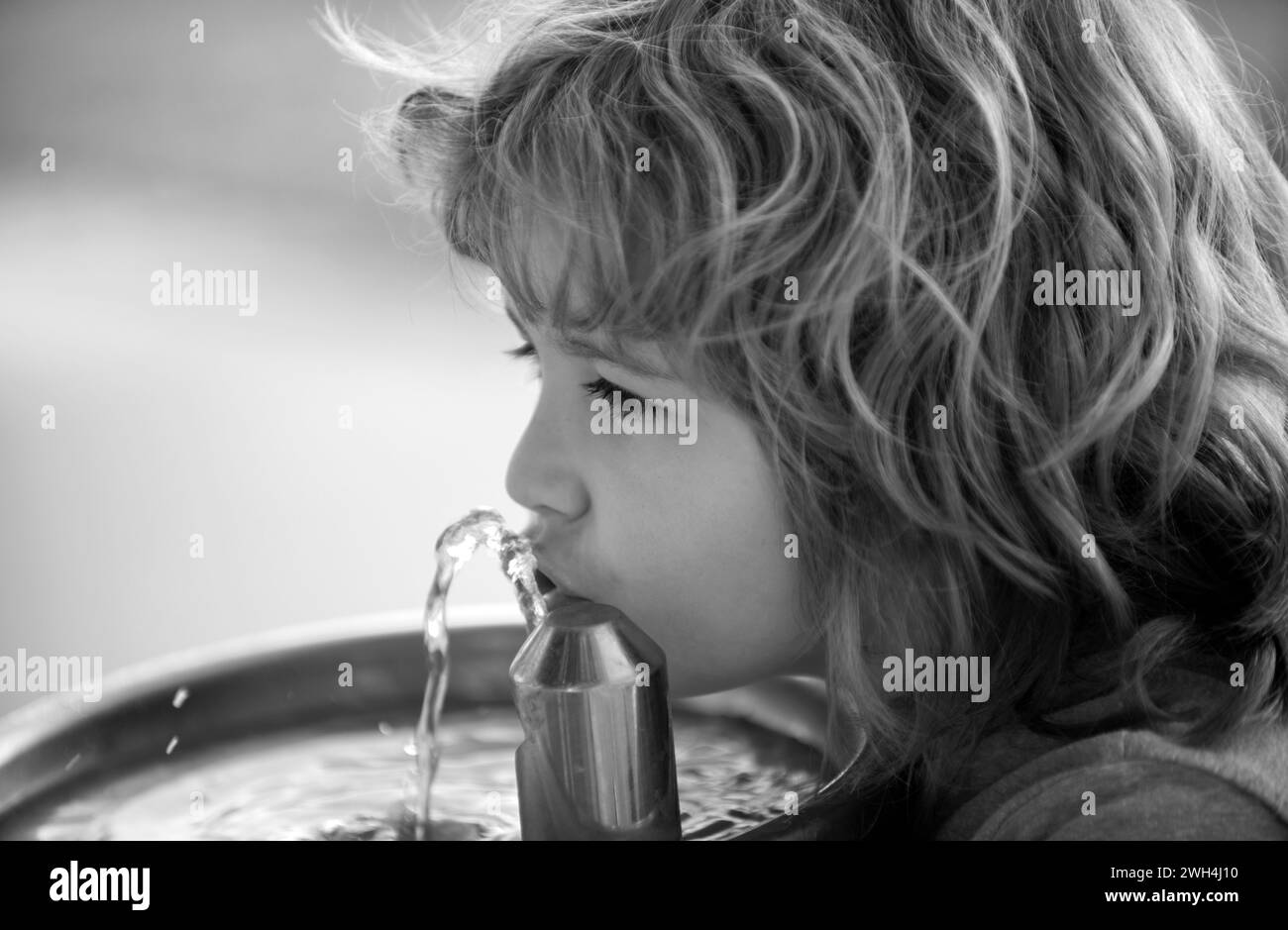 Kid drinking water from a water fountain in park. Thirsty child. Stock Photo