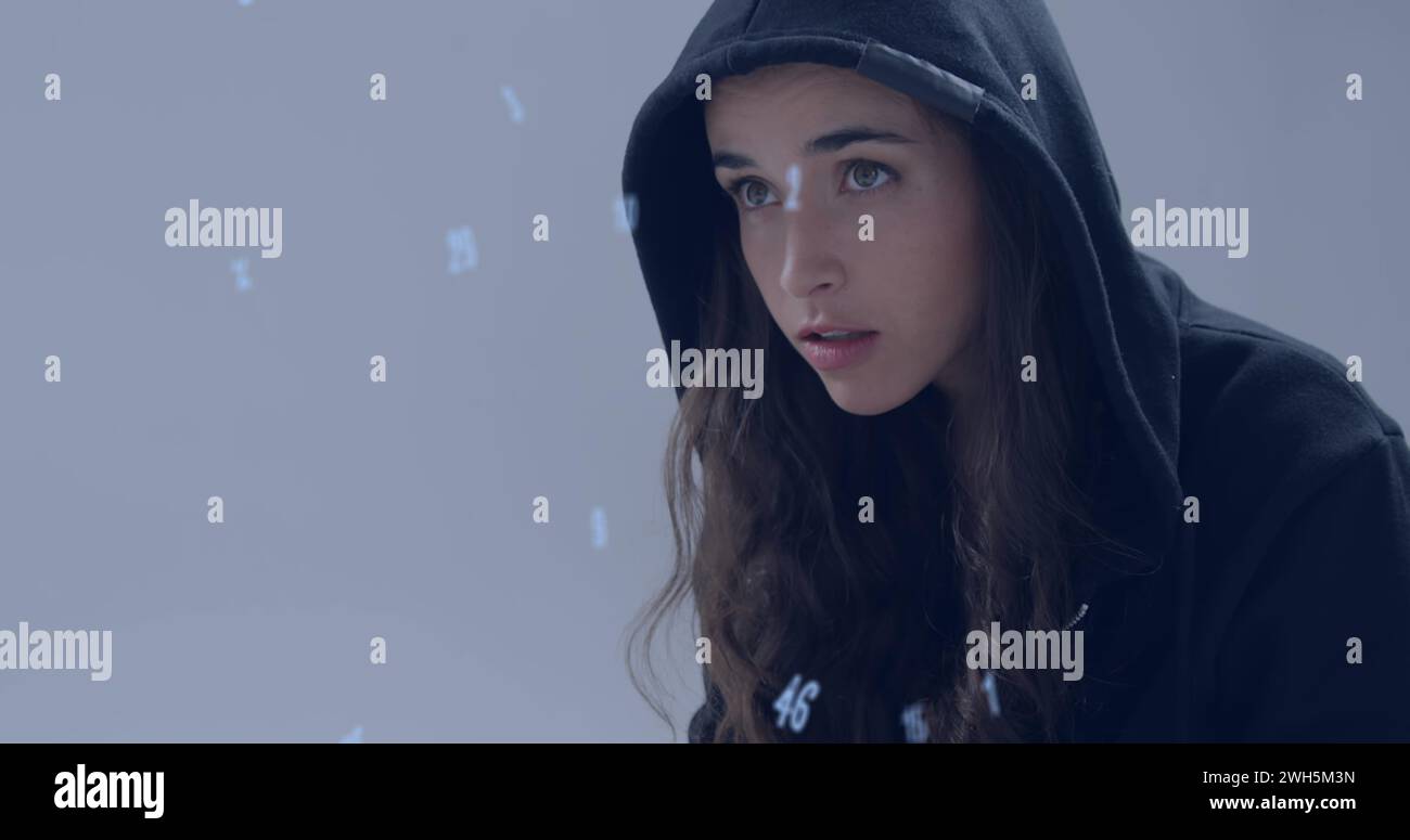 Image of numbers over caucasian hacker using computer Stock Photo