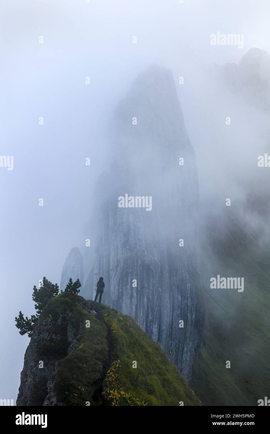 A hiker standing in front of the famous Swiss Alps peak Saxer Lucke with stunning rock formation in rising mist and fog Stock Photo