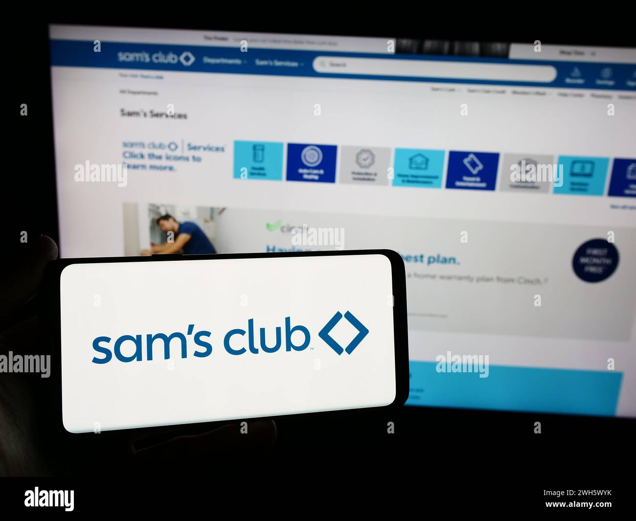 Person holding smartphone with logo of US membership-only retail stores company Sam's Club in front of website. Focus on phone display. Stock Photo