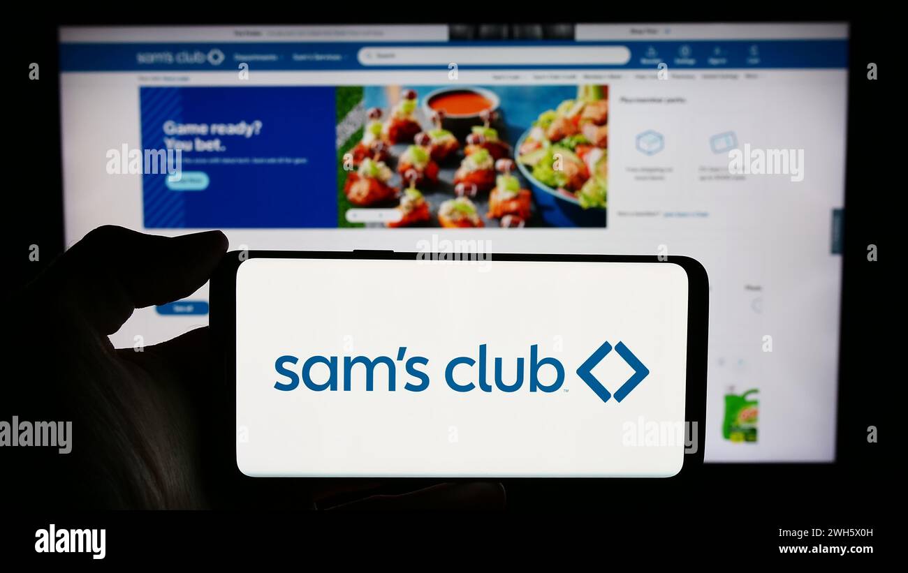 Person holding cellphone with logo of US membership-only retail stores company Sam's Club in front of business webpage. Focus on phone display. Stock Photo