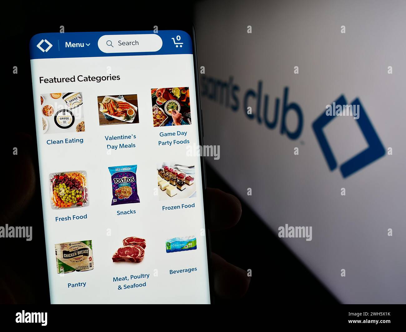 Person holding cellphone with web page of US membership-only retail stores company Sam's Club in front of logo. Focus on center of phone display. Stock Photo