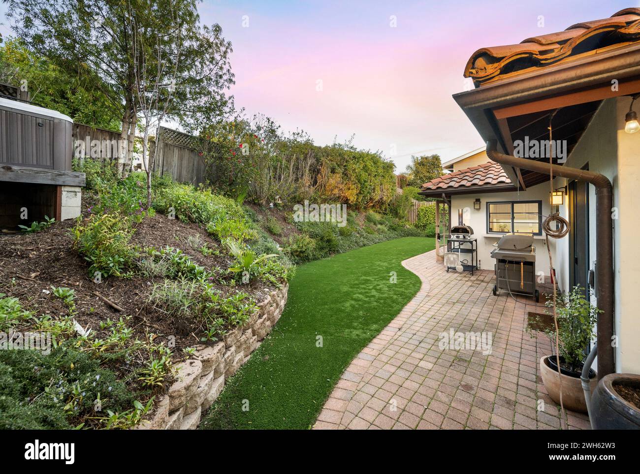 A backyard featuring a charming patio with a BBQ grill and verdant lawn Stock Photo