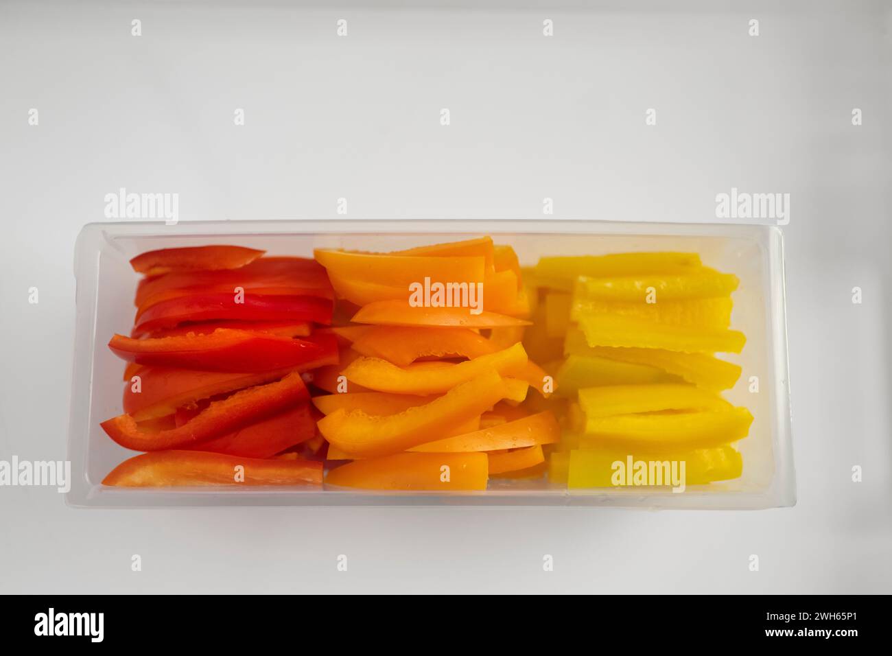 A top view of Julienne sliced colorful bell peppers in a clear plastic tub on a white tray Stock