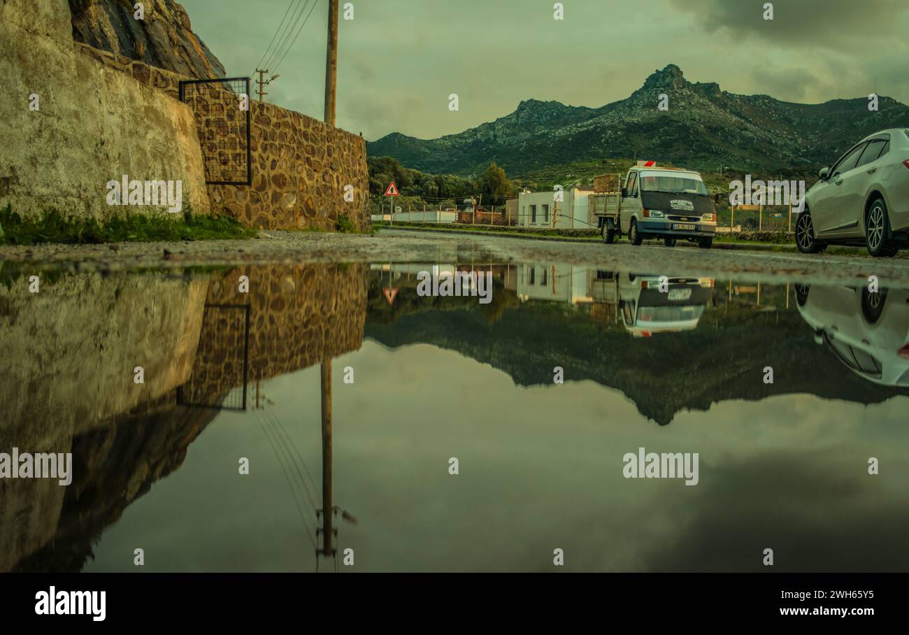 In the rainy village, a reflective scene unfolds on the wet road—cars, mountains, and village life captured in the serene beauty of rainy weather. Stock Photo