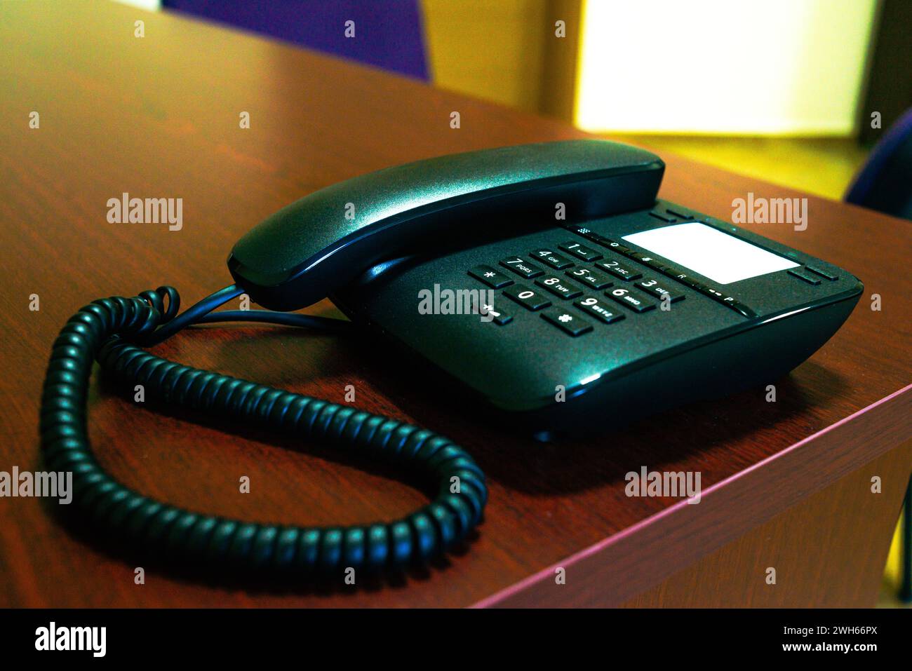A sleek black phone and its handset rest on a desk, embodying modern communication technology in a contemporary office workspace. Stock Photo