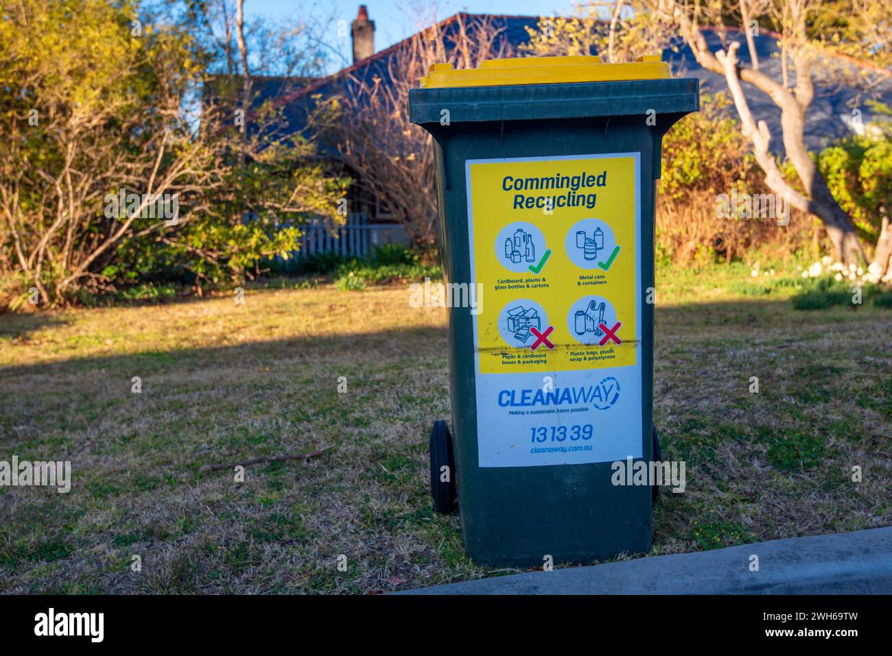 A yellow lid co-mingled recycling Sulo bin sits on a footpath awaiting collection by the contract recycling company Cleanaway Limited in NSW Australia Stock Photo