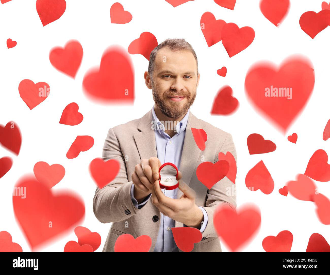 Man standing under falling hearts and holding an engagement ring in a box isolated on white background Stock Photo