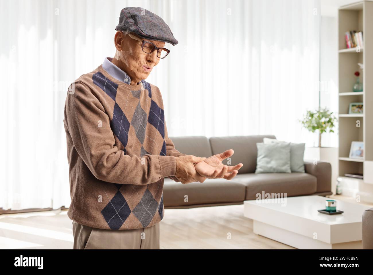 Elderly man in pain holding his wrist at home in a living room Stock Photo