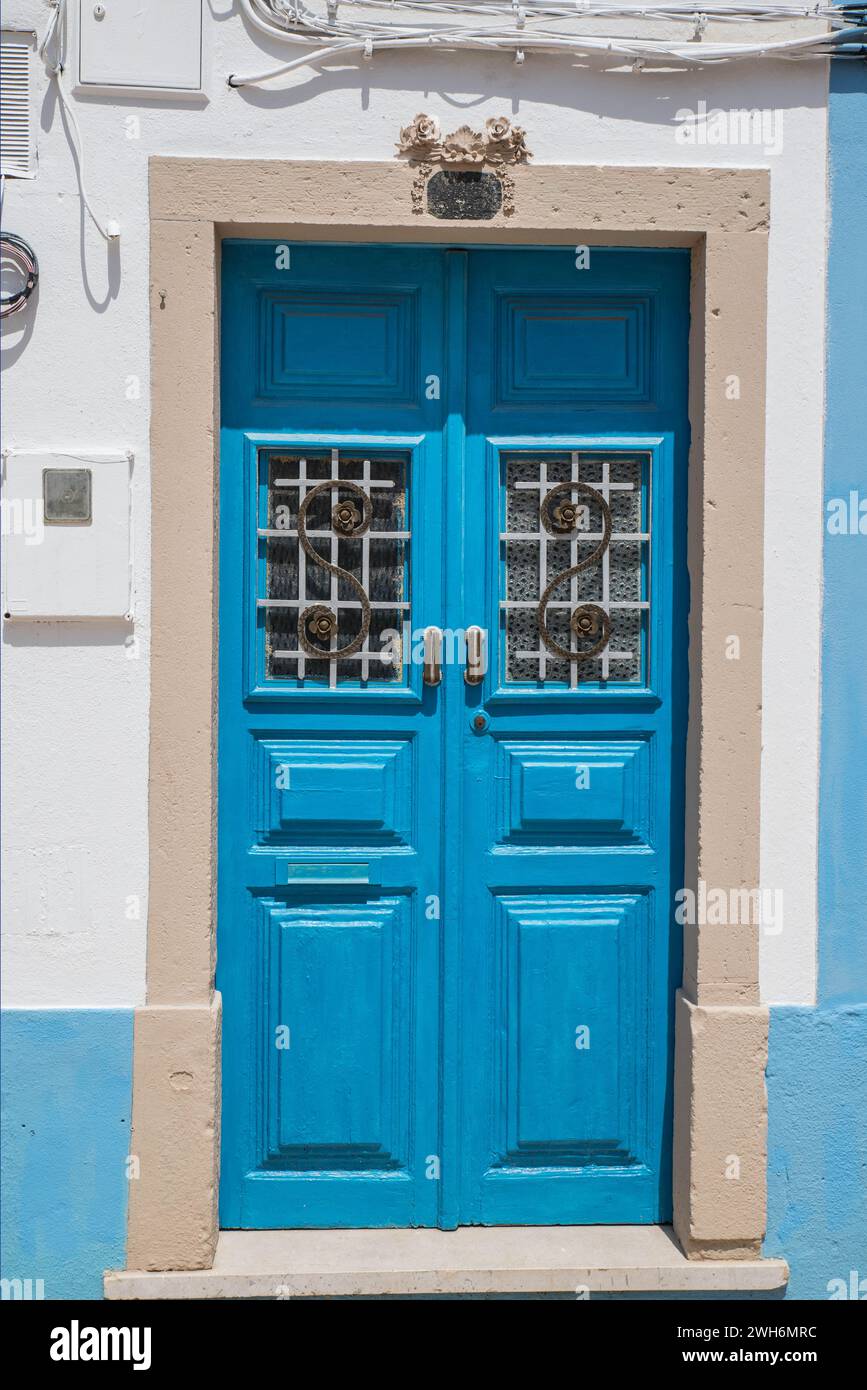An old wooden blue double door with glass panels and scrollwork in Lagos, Portugal Stock Photo