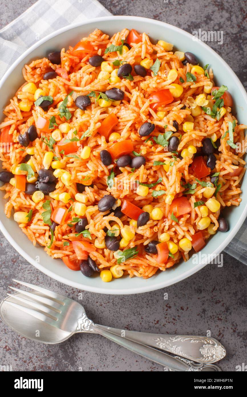 Mexican tomato rice with black beans, onions and corn close-up in a bowl on the table. Vertical top view from above Stock Photo