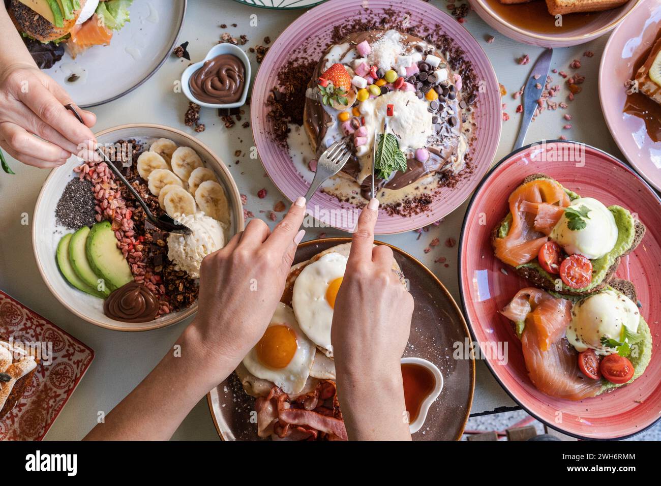 Breakfast is served with various dishes including eggs, bacon, pancakes and fruits on a colorful table. Stock Photo
