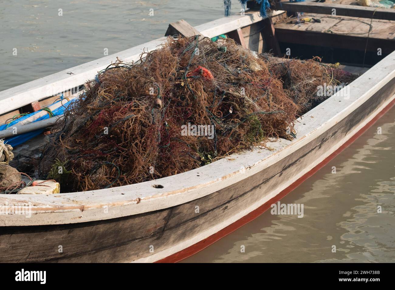 A pile of fishing nets and seaweed on a boat on a pier Stock Photo
