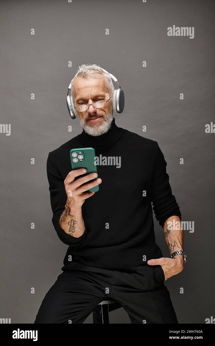 good looking mature male model with beard and headphones in black turtleneck looking at phone Stock Photo