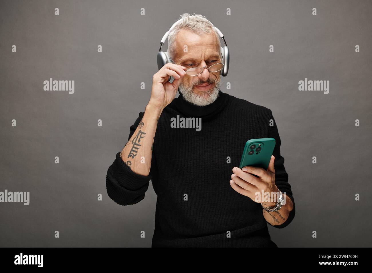good looking mature male model with beard and headphones in black turtleneck looking at phone Stock Photo