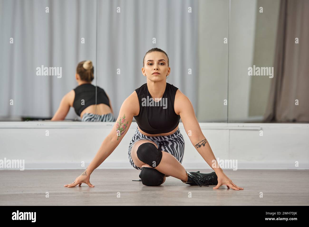 A graceful woman gracefully performs a choreographed dance on the floor in studio with mirror Stock Photo