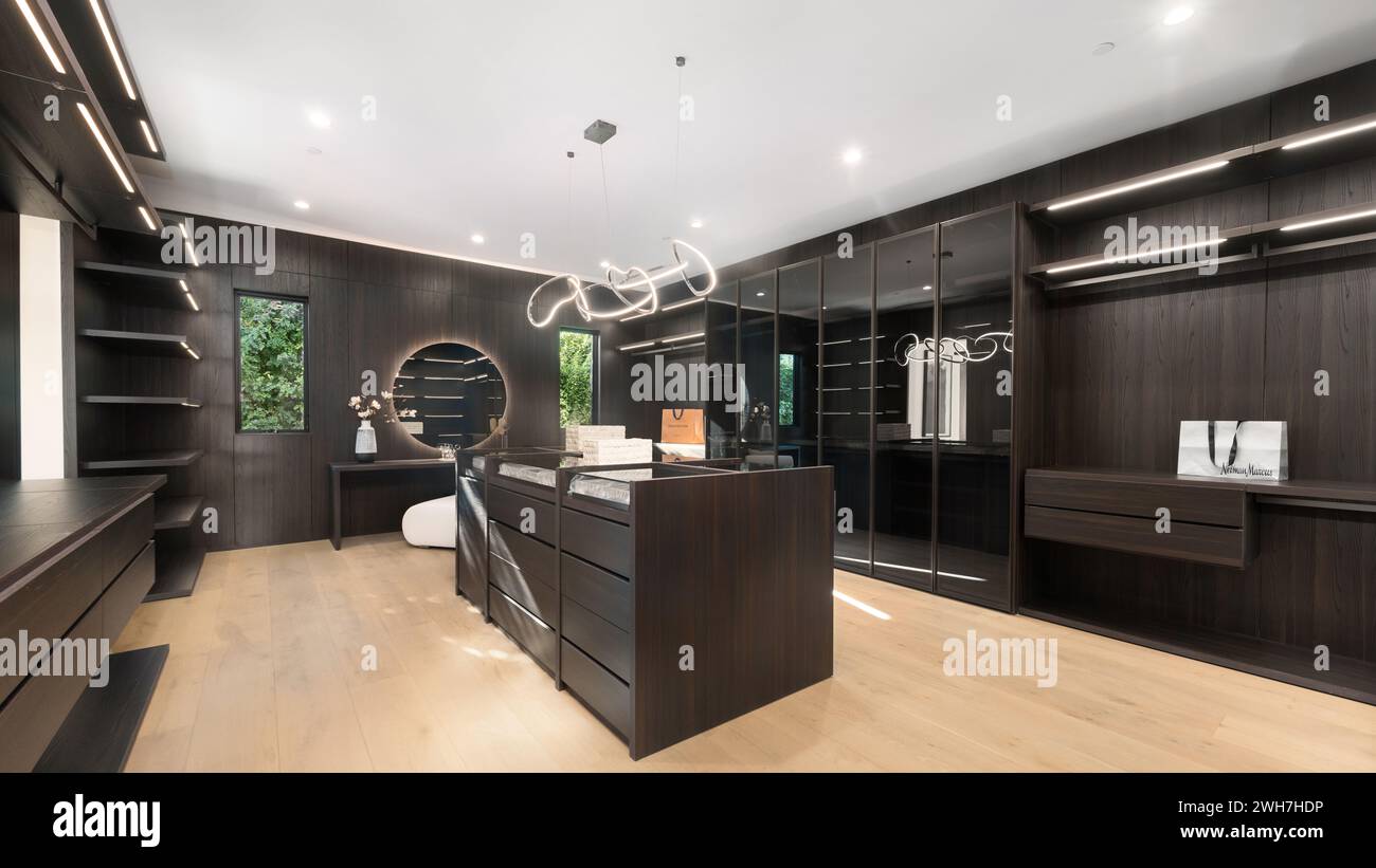 A stylish walk-in closet featuring elegant wooden cabinets and drawers Stock Photo