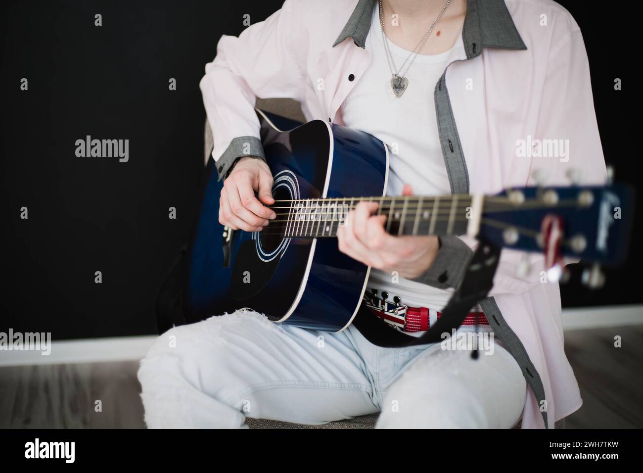 A young slim attractive man in white shirt playing  blue guitar on black  background, close up Stock Photo