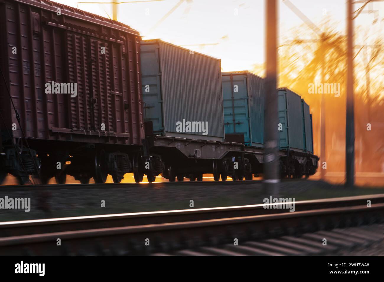 Freight train traveling by railroad with blur effect at sunset. Freight train transportation. Industrial style. Stock Photo