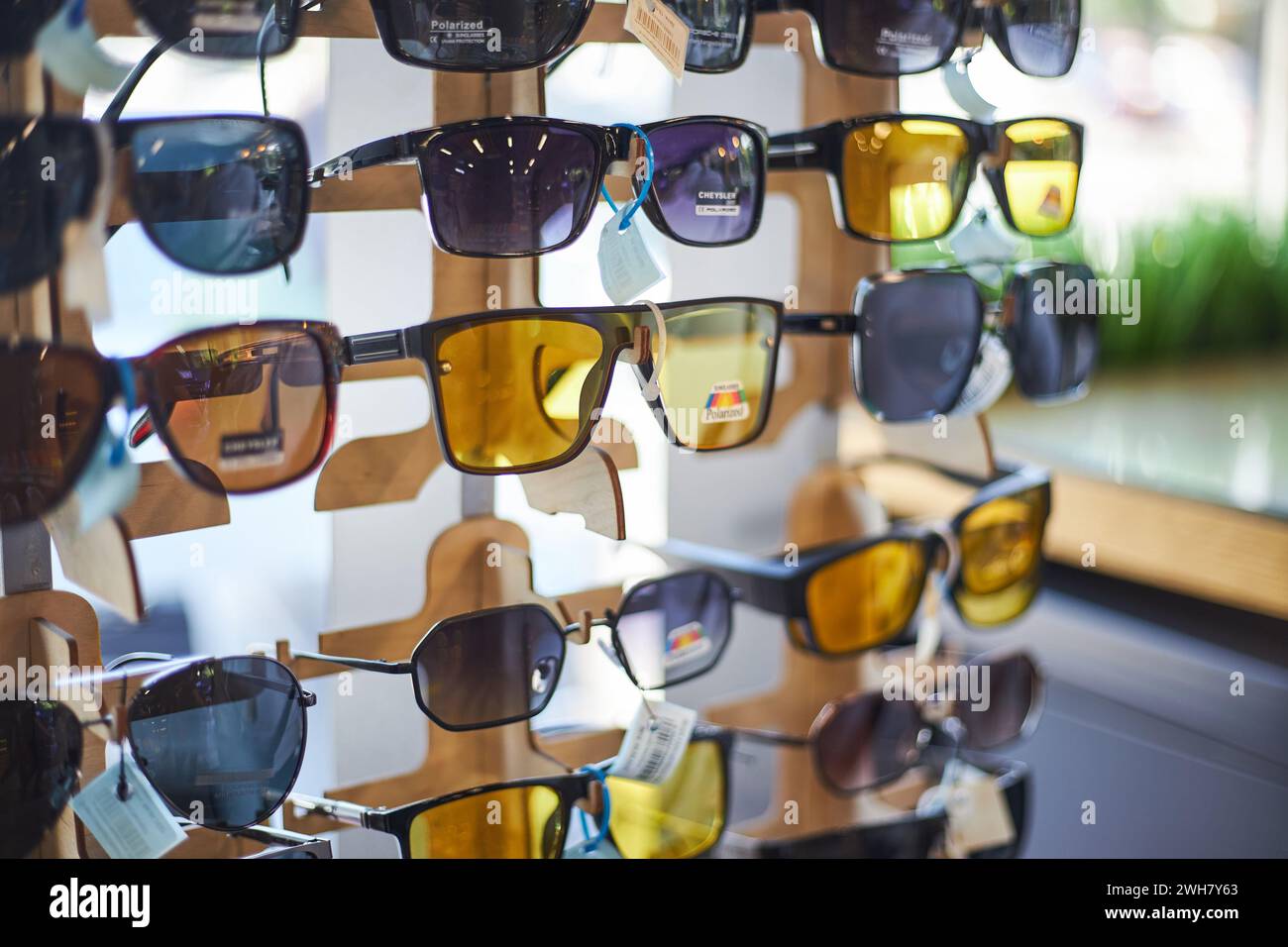 Rack in a store with lot of sunglasses in dark gray and yellow colors for driving. Optical shop, eye care. Bishkek, Kyrgyzstan - 26 May 2023. Stock Photo