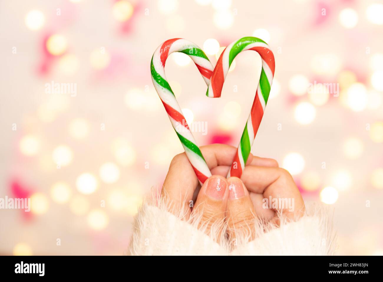 woman hand with sweater holding candy canes in the shape of heart, defocus bokeh light decorate for Valentine's Day celebration at background. Stock Photo