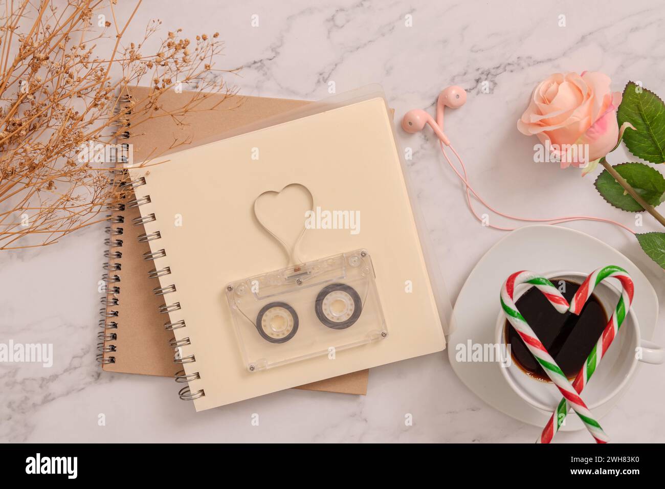 vintage transparent audio cassette with magnetic tape in shape of heart on blank book page, candy canes in the shape of heart on coffee cup, earphones Stock Photo