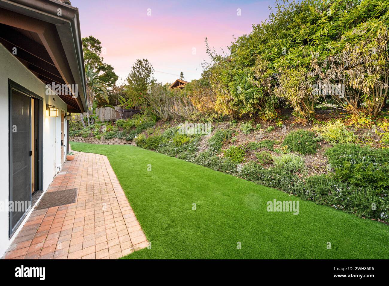 Brick paver patio surrounded by lush foliage in backyard of a residential home Stock Photo