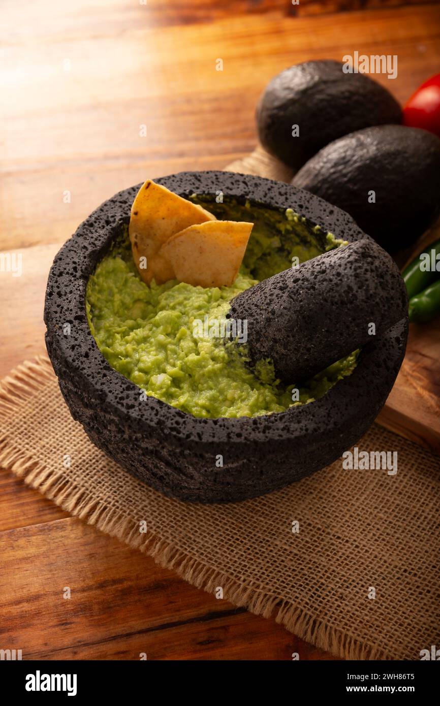 Guacamole. Avocado dip with tortilla chips also called Nachos served in a bowl made with volcanic stone mortar and pestle known as molcajete. Mexican Stock Photo
