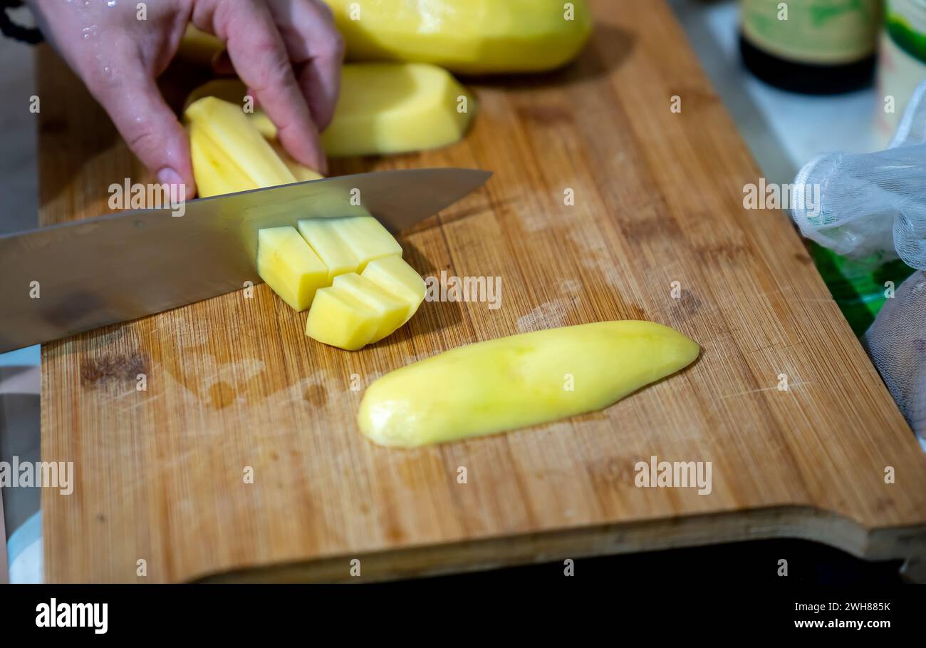 A person skillfully cuts up vibrant yellow vegetables on a rustic wooden board using a sharp knife Stock Photo