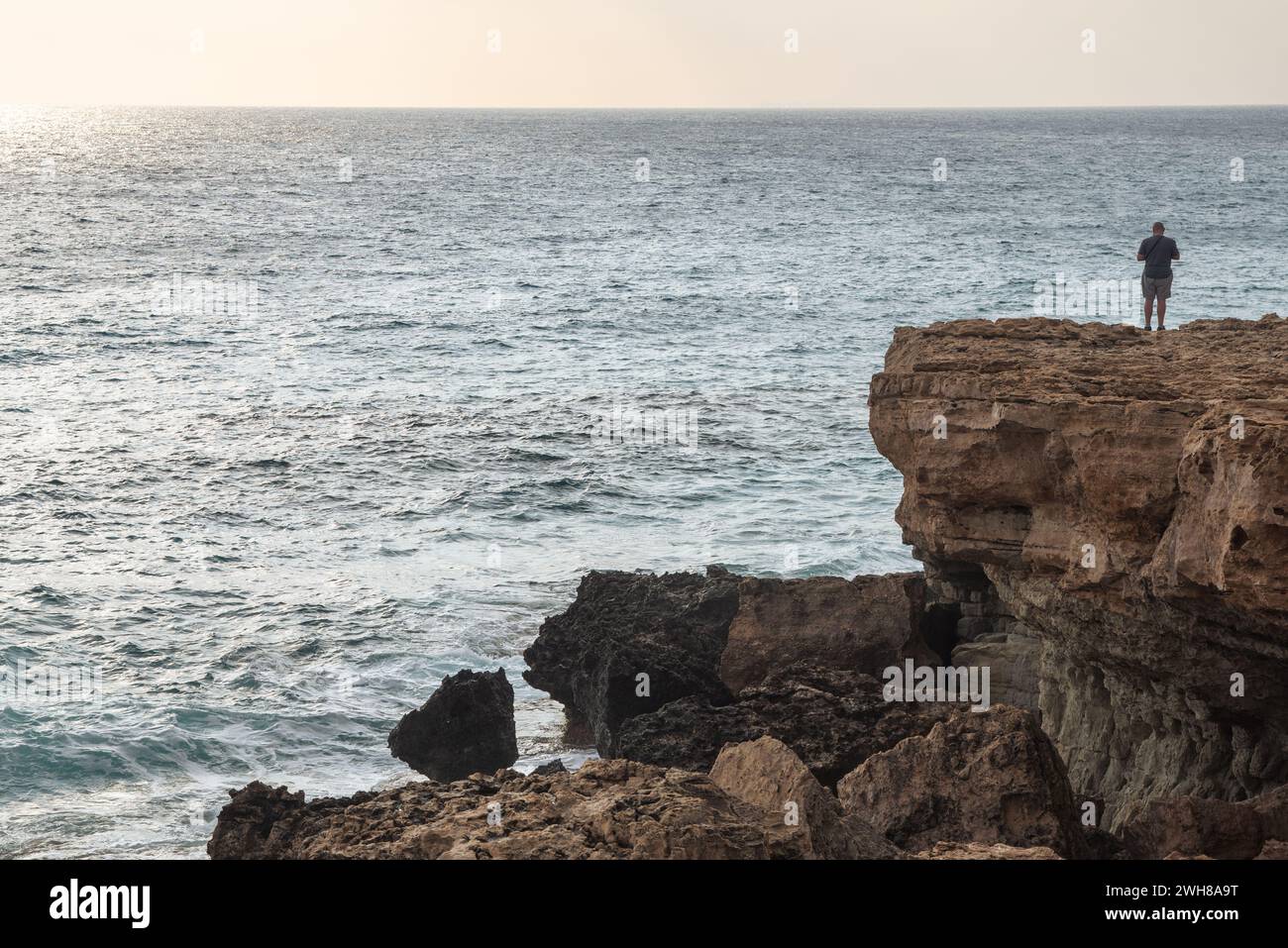 Unrecognized person standing at the edge of rocky coast sightseeing enjoying sunset Stock Photo