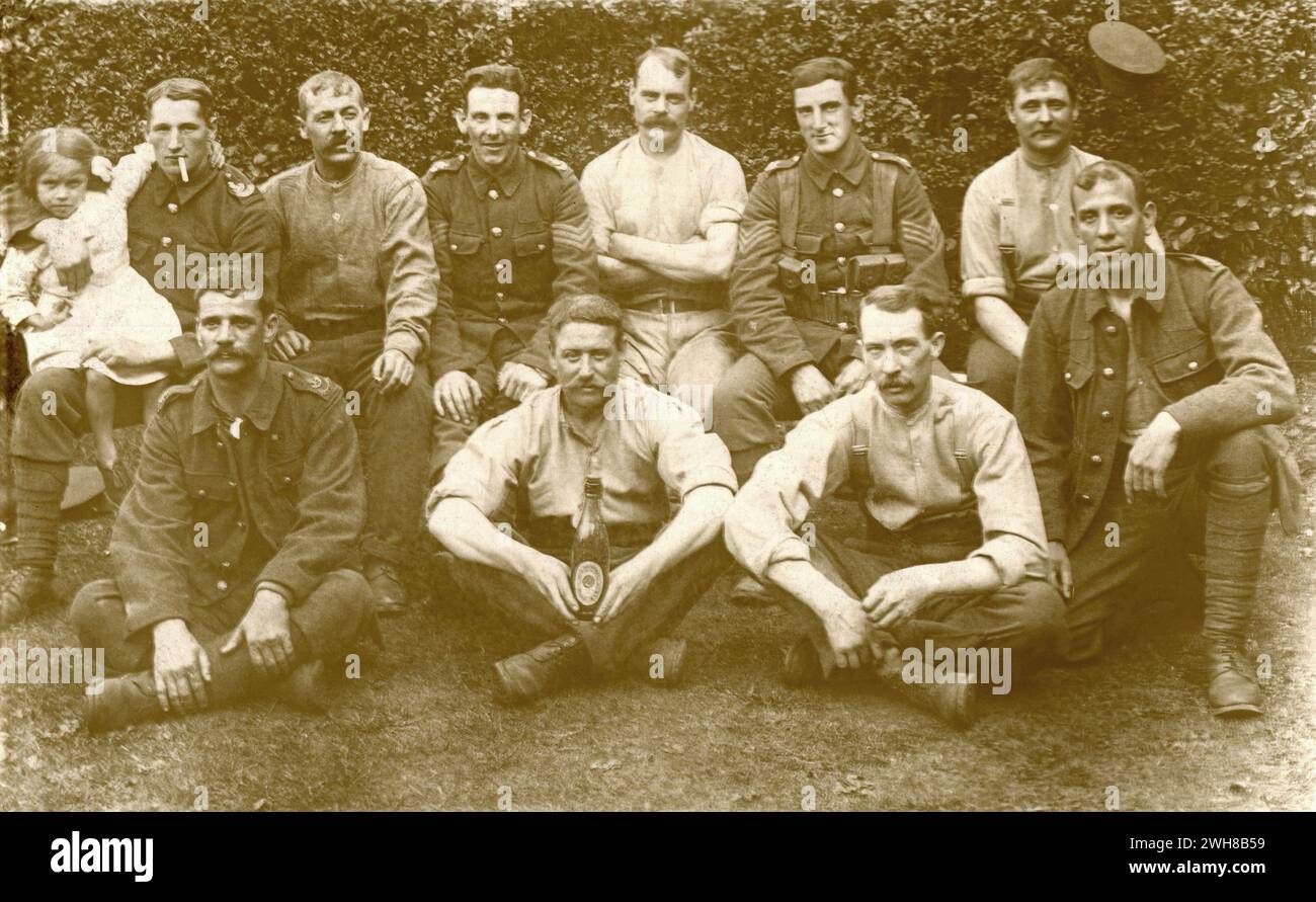 Yorkshire. 1914-1918 – An informal group photograph taken during the First World War, depicting British army soldiers of the Yorkshire Light Infantry Regiment.  The men are in uniform, some wearing their tunics, others just shirts. One soldier, a sergeant, is also wearing webbing. Another, who has a cigarette in his mouth, has his young daughter sat on his lap. The man in the centre foreground is holding a large bottle of Mild Ale beer. An army cap is hung on the hedge behind them. Stock Photo