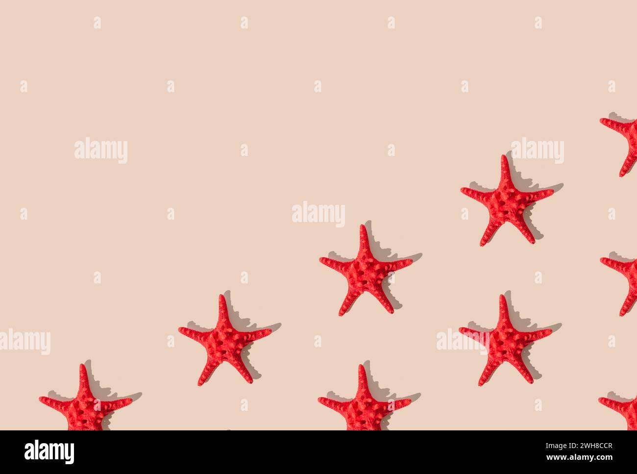 Summer pattern composition made with red starfish on sandy color background. Minimal summer concept. Creative sea star flat lay pattern idea. Stock Photo