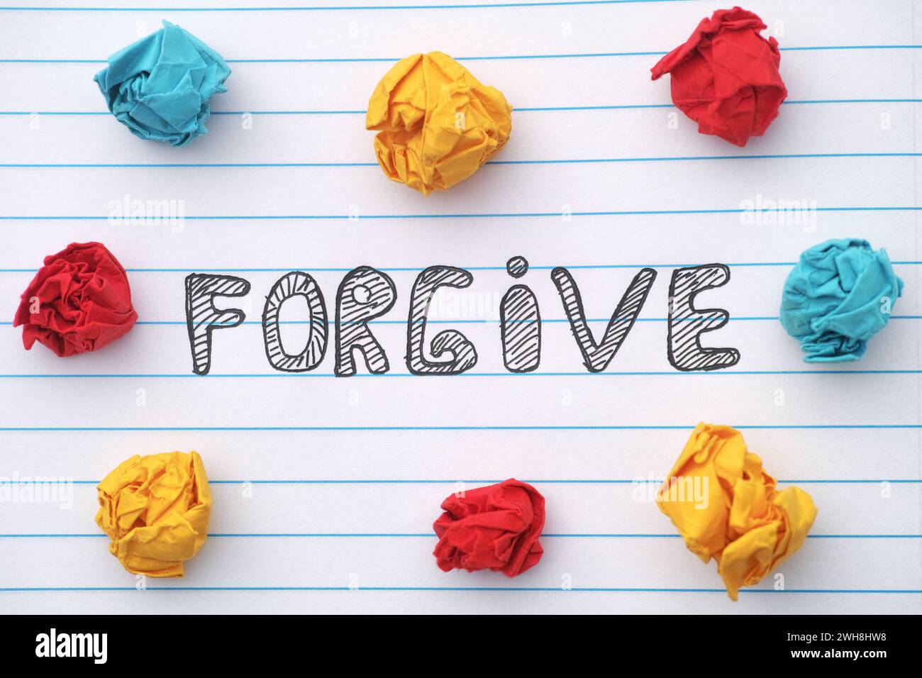 Forgive. The word Forgive written on a notebook sheet with some colorful crumpled paper balls around it. Close up. Stock Photo