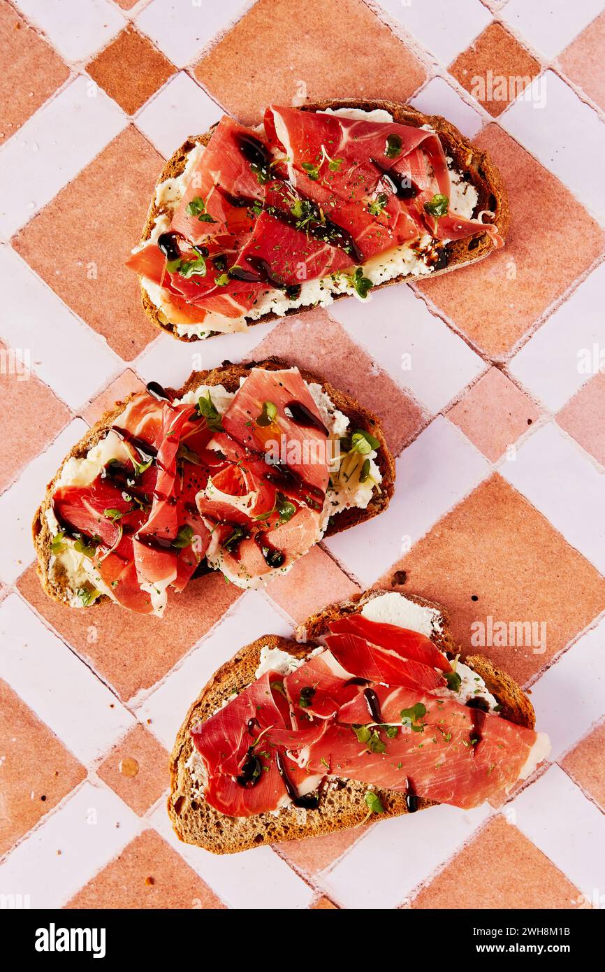 Ricotta and Parma Ham Toast with Balsamic Drizzle and Cress on a tiled background Stock Photo