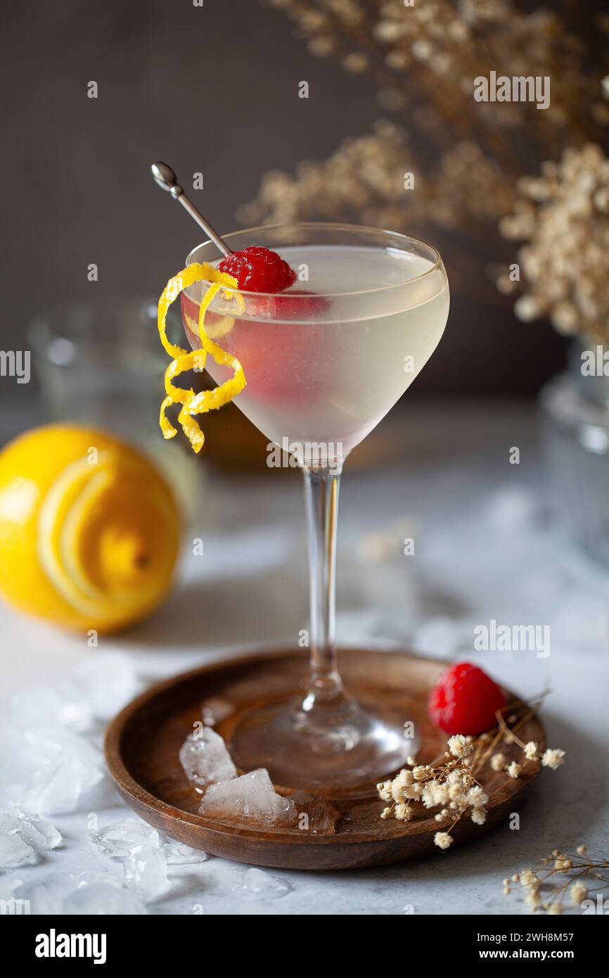 A vodka and limoncello cocktail in a Nick and Nora glass garnished with lemon zest and fresh raspberries. Stock Photo