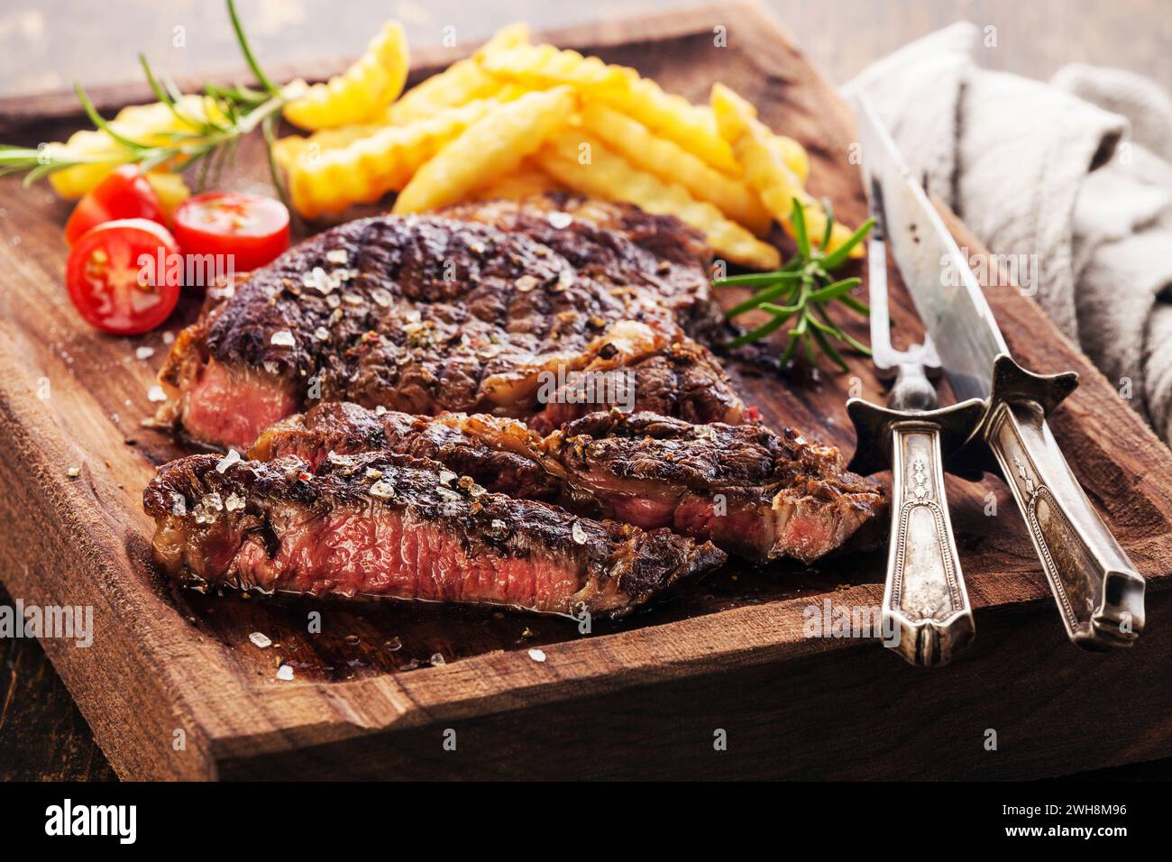 Sliced medium rare grilled Steak Ribeye Black Angus with french fries on serving board block Stock Photo